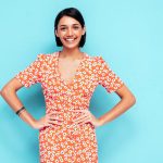 Young beautiful smiling female in trendy summer red dress. Sexy carefree woman posing near blue wall in studio. Positive model having fun. Cheerful and happy. Isolated